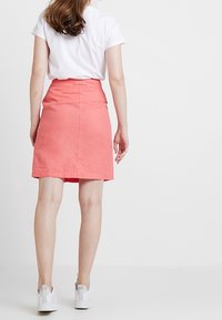 Rok panjang lutut berwarna koral dengan pinggang yang pas, potongan lurus, dan tekstur halus, dipadukan dengan kaos putih lengan pendek dan sneakers putih.