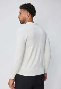 Pull tricoté blanc à manches longues, avec une texture côtelée verticale et un col à revers. Finition lisse et coupe ajustée.