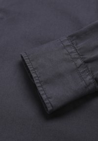 Material de cămașă din bumbac de un albastru închis, având un manșon pliat cu un tiv cusut curat, textură netedă și fără modele sau accente vizibile.