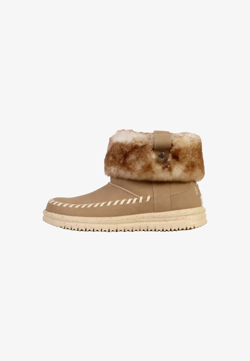 Botín beige con un puño de pelo sintético, detalles de costura y una suela de goma texturizada. Presenta una tira lateral con un botón metálico circular.