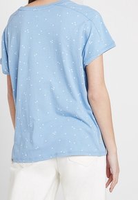 Ljusblå kortärmad skjorta i bomull med ett spritt blommönster och en avslappnad passform, rund halsringning och uppvikt ärmslut.