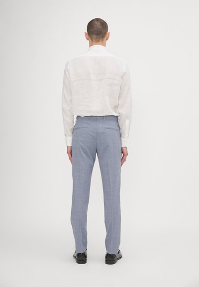 Camicia bianca in lino a maniche lunghe con vestibilità rilassata, abbinata a pantaloni su misura azzurri chiari con un sottile motivo a scacchi e tasche posteriori.