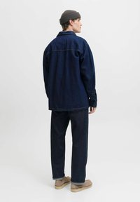 Camicia in denim scuro e pantaloni abbinati, caratterizzati da una vestibilità rilassata, maniche lunghe e tasche laterali. Indossata con un berretto grigio a costine e scarpe beige.
