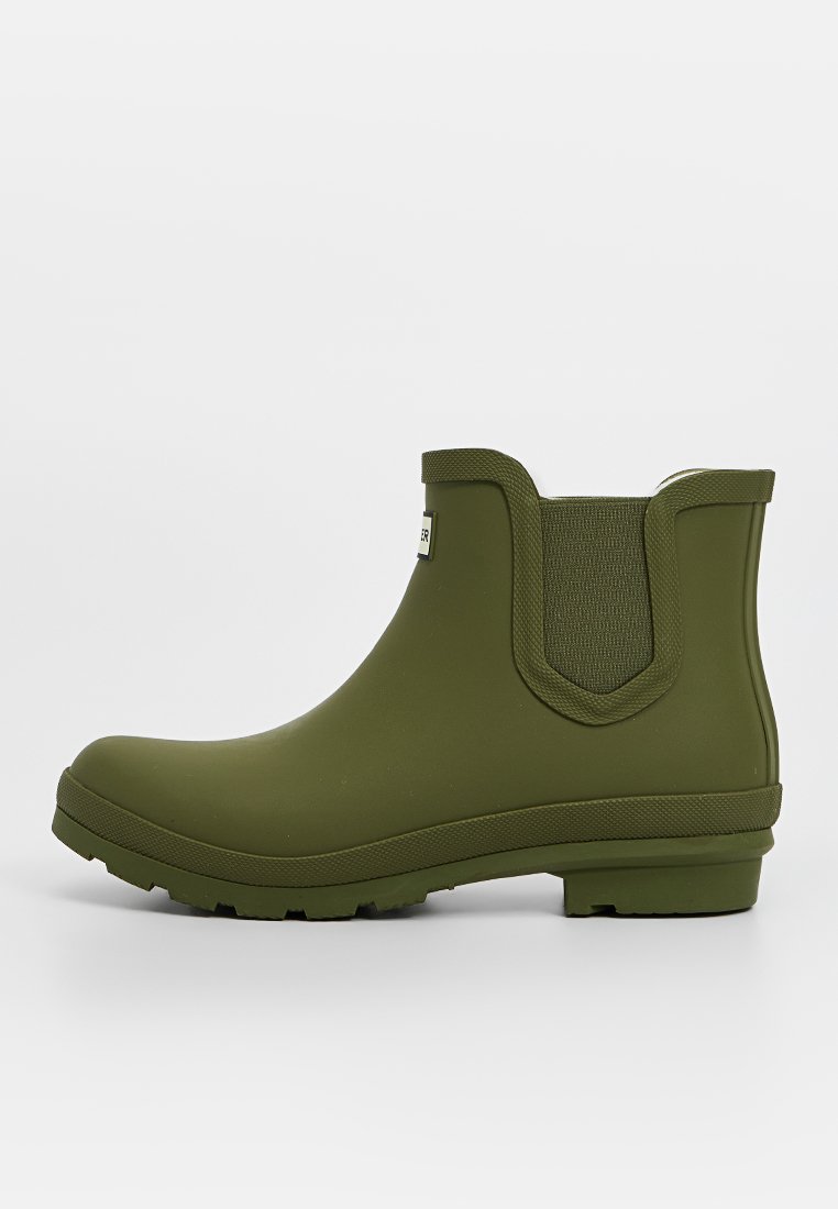Grüne Gummistiefel über den Knöcheln mit elastischen Seiteneinsätzen, glatter Textur und einem niedrigen Blockabsatz, mit einem Logofähnchen auf der Vorderseite.