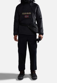 Black insulated pullover jacket with zippered pocket, featuring a logo and Norwegian flag. Paired with dark cargo pants and black boots.