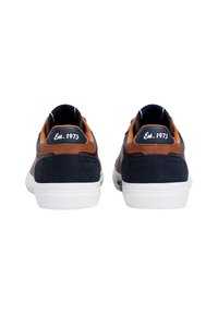 Tengerészkék és barna bőrszövet sportcipők fehér talppal, lekerekített dizájnnal és "Est. 1973" hímzéssel a hátsó részen.