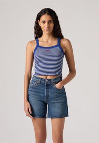 Mėlynai ir baltai dryžuotas trumpas tank topas su storais petnešomis, derinamas su aukšto liemens mėlynais džinsiniais šortais su sagų uždarymu ir kišenėmis.