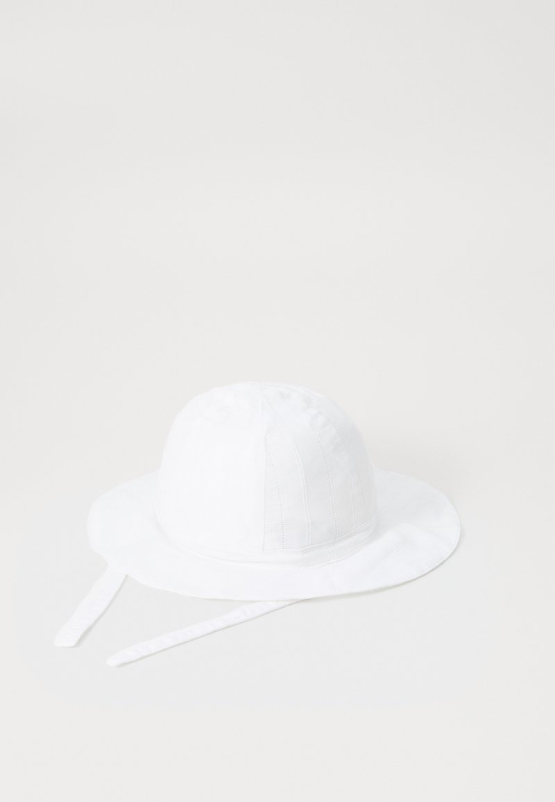 Baltas audinio skrybėlė su minkšta tekstūra. Ji turi plačią kraštą, vertikalias siūles ir dvi reguliuojamas raištas tvirtam prisitaikymui.