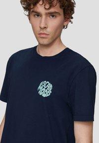 Navyblauwe katoenen t-shirt met een cirkelvormige mintgroene "ESCAPE MOOD" graphic op de linkerborst. Korte mouwen en ronde hals.