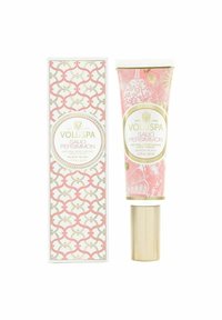 Voluspa Saijo Persimon handkräm i en rosa blommig tub med guldaccent, bredvid en mönstrad rosa och vit låda, båda med eleganta mönster.