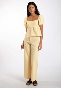 Haut en peplum à manches bouffantes, texturé et à carreaux jaunes, associé à un pantalon large assorti. Porté avec des sandales à lanières noires.