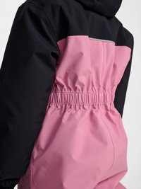 Set bagfra af sort og pink jakke med elastisk talje og reflekterende stribe på øvre ryg, båret med hætten oppe.