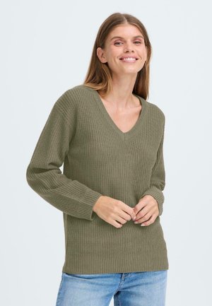 Pull en v olive avec un motif de tricot texturé et des manches longues, présentant des poignets et un ourlet côtelés. Porté sur un jean bleu clair.