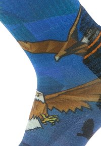 Knähöga strumpor med en blå bakgrund och illustrerade örnar i nyanser av brunt och kräm, tillverkade av ett mjukt, texturerat tyg.