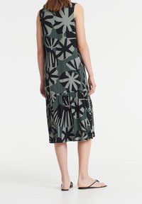 Bezramínková šaty s vícevrstvým designem v tmavě zelené a černé barvě s velkými abstraktními květinovými vzory. Vyrobené z lehkého materiálu, s plynulým střihem.