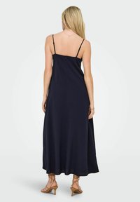 Robe maxi bleu marine avec de fines bretelles spaghetti, en tissu lisse et légèrement évasée à l'ourlet. Elle dispose d'une fermeture éclair dissimulée dans le dos.