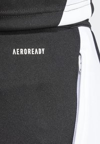 Svart atletisk tyg med vita accenter och en AEROREADY-logotyp. Har en slät textur och en detalj med dragkedja.