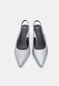 Talons slingback en argent pailleté avec un bout pointu, présentant des semelles intérieures en cuir noir et une texture lisse. Le logo de la marque est à l'intérieur de la chaussure.