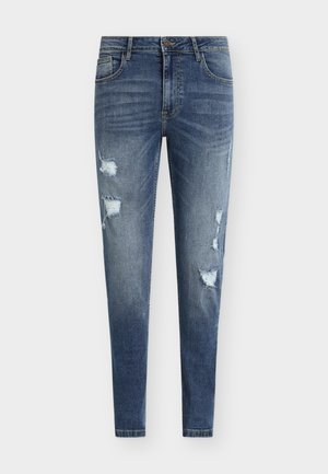 Modre ozke kavbojke iz jeansa z raztrganimi detajli, več razpokami in zbledelimi madeži. Imajo pet žepov in zanke za pas.