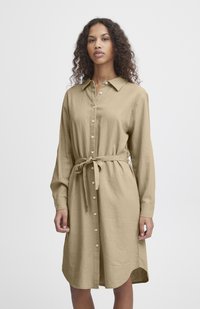 Rochie cămașă cu nasturi, din in de culoare bej deschis, cu mâneci lungi, guler și un cordon legat la talie. Prezintă o croială dreaptă și un tiv rotunjit.