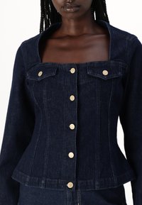 Giacca in denim scuro con un design aderente, scollatura quadrata e bottoni dorati. Presenta due tasche sul petto e un orlo peplum.
