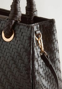 Sac à main en cuir tressé brun foncé avec poignées tressées et boucle métallique dorée fixant une bandoulière.