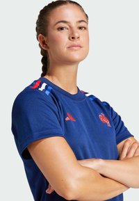 Navy blue athletic shirt with short sleeves, featuring red and blue stripes on shoulders and a red rooster logo. Made from breathable material.
