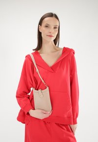 Rode hoodie met een V-hals en een voorzak, gecombineerd met een lichtbeige schoudertas met een drukknoopsluiting en textuurdetails.