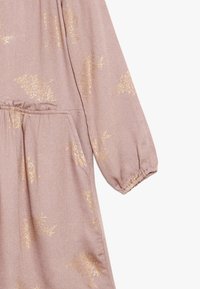 Svetle růžové šaty s dlouhými rukávy, zlatými třpytivými vzory, elastickým pasem a nařasenými manžetami rukávů. Měkká textura s volným střihem.