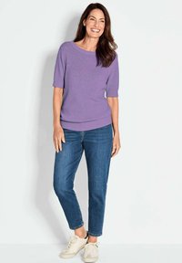 Lichtpaarse gebreide trui met korte mouwen, gecombineerd met blauwe jeans en crèmekleurige sneakers. Soepele textuur, relaxte pasvorm en ronde halslijn.