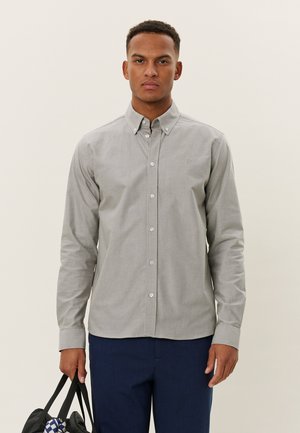 Lange mouw blouse in lichtgrijs met subtiele strepen, voorzien van een kraag en knoopsluiting aan de voorkant, gedragen met marineblauwe broeken.