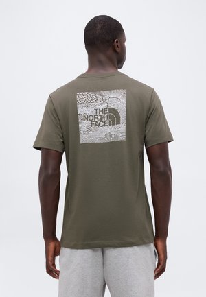 Homme portant un t-shirt vert olive avec un graphisme blanc et le logo "The North Face" dans le dos, associé à un short gris clair.