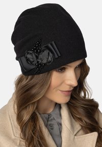 Gorro de lana negro con una textura suave, decorado con dos acentos florales y una cinta de satén, adornado con cuentas negras a lo largo del lado.