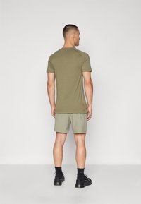 Olive green athletic t-shirt with short sleeves, paired with light khaki shorts. Smooth fabric with a regular fit. Black shoes and socks.