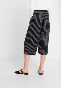 Svarta och vita randiga culotter med avslappnad passform, som har resårmidja och fickor. Stylad med svarta slip-on skor.