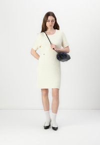 Robe crème, à manches courtes avec un tissage texturé. Accentuée d'un petit détail doré, associée à un sac à main noir et des escarpins en vernis.