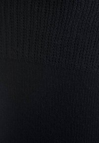 Tessuto a maglia a coste nero con una texture morbida, caratterizzato da linee verticali e un bordo superiore liscio. Il colore è uniforme e di un nero intenso.