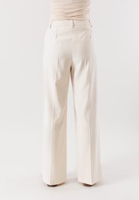 Pantaloni larghi color crema con una texture liscia, dotati di tasche posteriori e una vita strutturata. Progettati per una vestibilità rilassata.