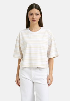 Young woman with straight dark hair wearing a white and beige striped oversized T-shirt and white pants, facing forward.