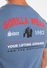 Blauwe katoenen T-shirt met opvallende rode en witte tekst op de achterkant, een gorilla-afbeelding en een klassieke ronde halsuitvoering.