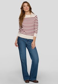 Gestreifter Pullover in Creme mit kastanienbraunen Linien, mit Bootsausschnitt und zwei Knöpfen. Kombiniert mit blauen Schlagjeans und braunen Schuhen.