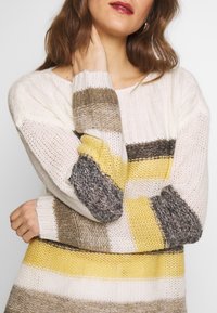 Maglione lavorato a maglia con ampie righe in bianco, beige, giallo e grigio. Presenta una vestibilità ampia e polsini a costine, con un filato texture.