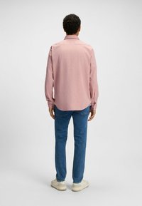 Rood geruit overhemd met lange mouwen en een geknoopte kraag, gedragen met blauwe spijkerbroeken en lichtgekleurde sneakers. Gladde stof met een relaxte pasvorm.