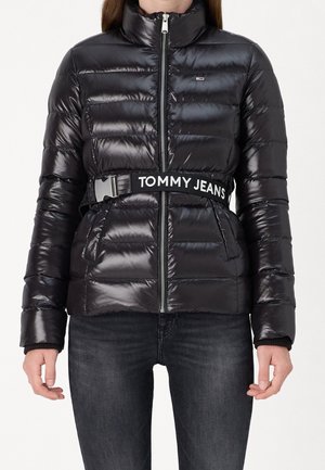 Doudoune noire brillante avec zip devant, poches latérales et une large ceinture noire marquée "TOMMY JEANS", portée avec un jean foncé.