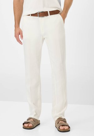 Pantalons en lin blancs avec une coupe droite, ornés d'une ceinture en cuir marron et portés avec des sandales en daim marron.