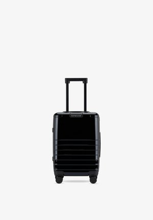 Valise rigide noire avec poignée télescopique, quatre roues pivotantes et rainures horizontales, étiquetée « Kapten & Son » en haut au centre.