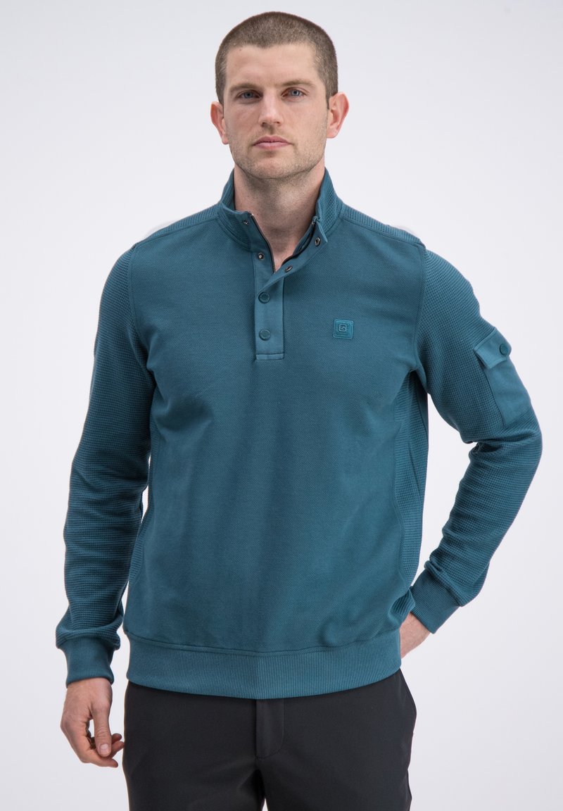 Morski pulower z teksturowanym korpusem i gładkim kołnierzem, z trzema guzikami przy dekolcie i boczną kieszenią. Żebrowane mankiety i dół.