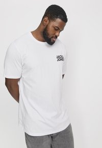 Biela bavlnená tričko s okrúhlym výstrihom, krátkymi rukávmi a čiernym logom "JACK & JONES" na ľavom hrudníku. Štandardný strih.