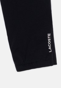 Juoda medvilnė jogger tipo kelnės su elastinėmis rankogaliais. Šone yra baltas "LACOSTE" logotipas. Struktūruotas paviršius su paprastu dizainu.