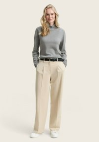 Grauer Strick-Turtleneck-Pullover kombiniert mit beigen, hoch taillierten, gefalteten Hosen, einem schwarzen Ledergürtel und weißen Sneakern; minimalistisches Design.